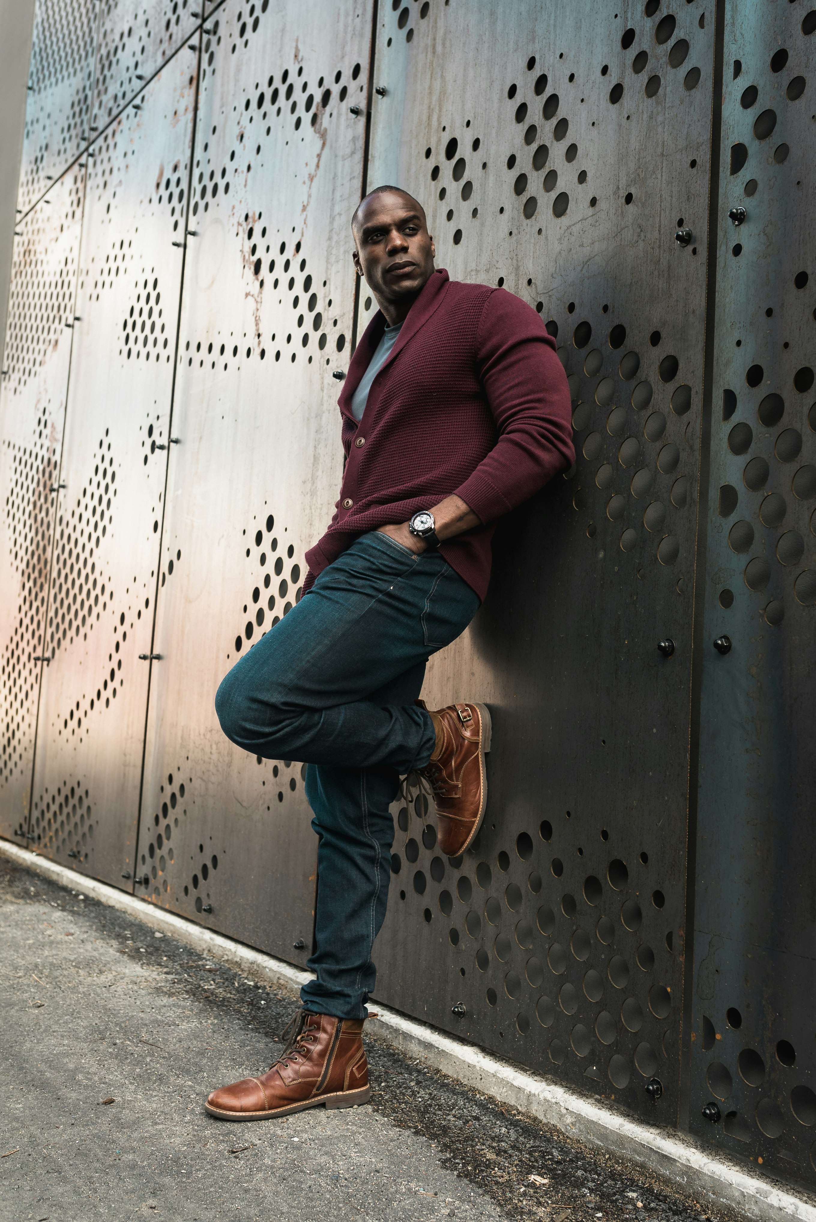 man in maroon long sleeve shirt and blue denim jeans sitting on black metal door